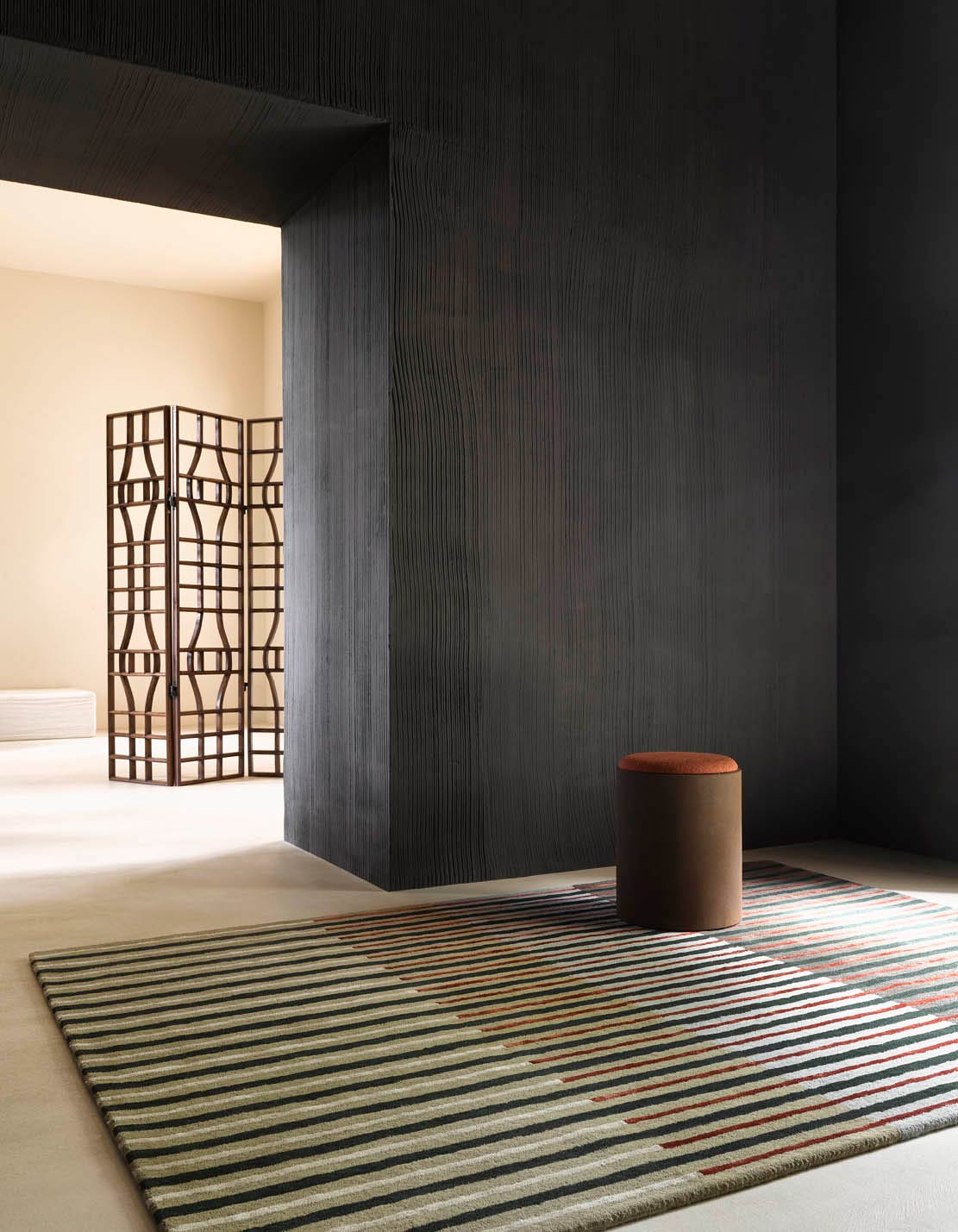 Nowoczesny dywan w pasy w minimalistycznym wnętrzu z ciemną ścianą i designerskim taboretem